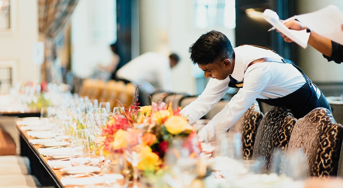 Waiter arranging flowers at a dining table.