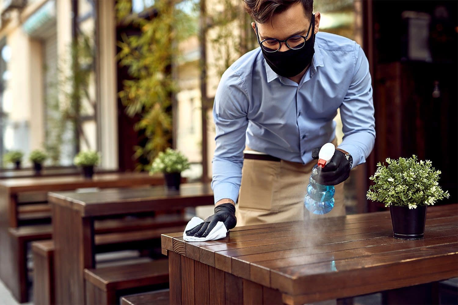 Person sanitizing outdoor table with spray