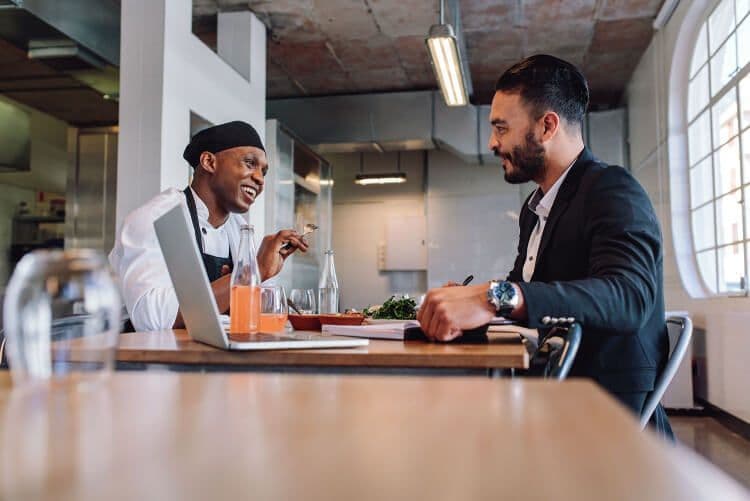 Chef and businessman discussing in restaurant kitchen.