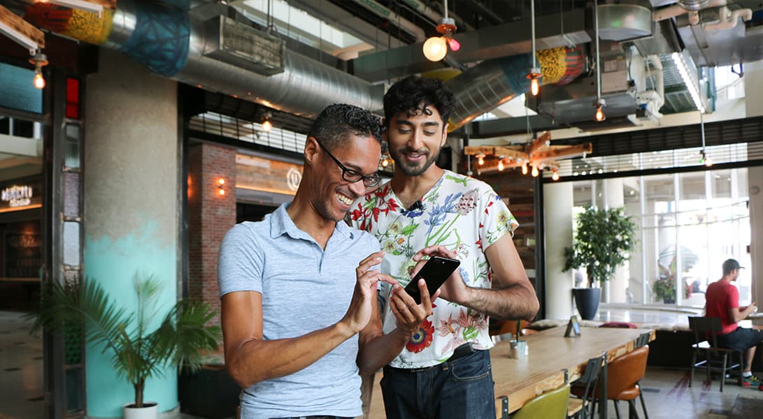Two people smiling, looking at a phone in cafe.