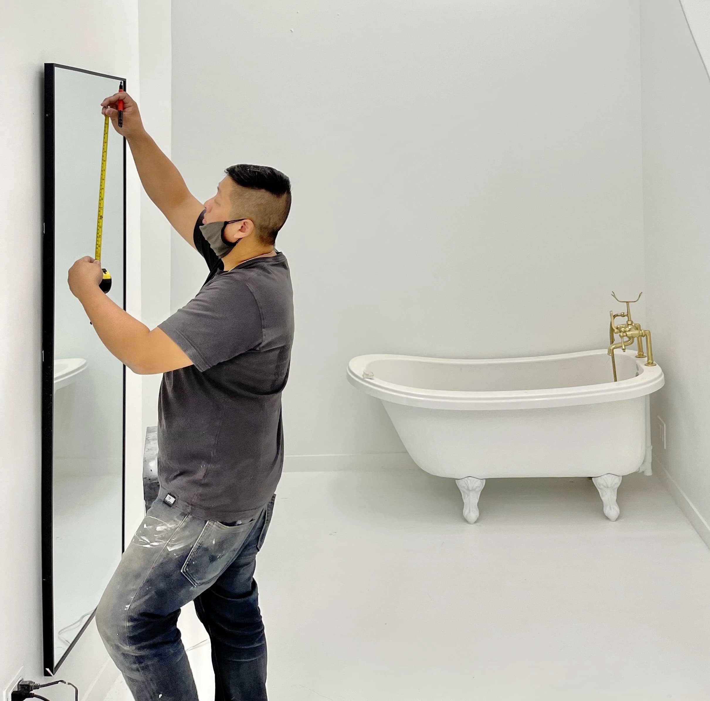 Man measuring mirror in bathroom with clawfoot tub.